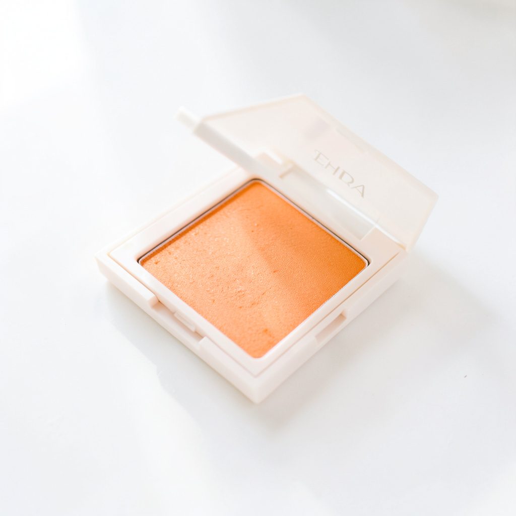 A neutral eyeshadow palette with warm caramel and bronze pans arranged on a pale linen surface in airy daylight